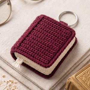 Può includere: Un portachiavi a forma di libro in miniatura realizzato in filato bordeaux scuro con pagine color crema e una piccola nappa segnalibro color crema. L'oggetto all'uncinetto presenta un robusto anello in metallo argentato sul dorso.