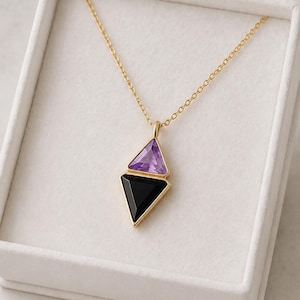 Op de afbeelding: Een gouden ketting met een hanger bestaande uit twee gestapelde driehoekige edelstenen. De bovenste steen is een lichtpaarse amethist en de onderste steen is een zwarte onyx. De hanger hangt aan een fijne gouden ketting in een doosje.