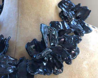 Puede incluir: Un collar negro iridiscente hecho de grandes cuentas de forma irregular, parecidas a conchas.