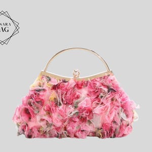 Puede incluir: Un bolso de mano floral rosa con asa dorada y cierre joya. El bolso está cubierto de capas de pétalos de tela rosa y blanca. El logotipo "LUNARA BAG" está en la esquina superior izquierda.