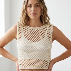 Puede incluir: Top de crochet sin mangas de color crema con un diseño de malla de rombos. El top se lleva sobre una prenda blanca. El cuello y el dobladillo están acabados con un borde de crochet sólido. Una prenda de verano ligera y aireada.