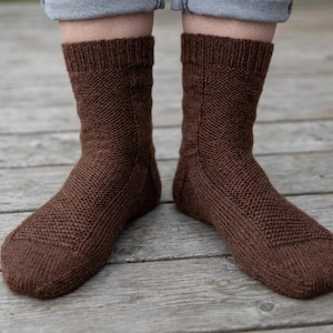 Puede incluir: Un par de calcetines marrones de punto. Los calcetines son de color marrón cálido y liso y tienen un diseño texturizado y estampado. Los calcetines se muestran en las piernas de una persona, con los puños de los calcetines visibles.
