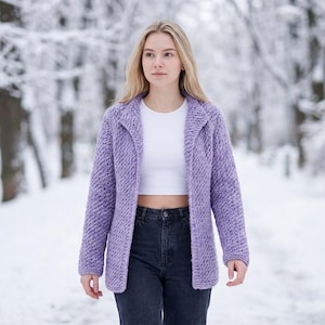 May include: A light purple, open-front cardigan with a textured knit pattern. The cardigan has a collared neckline and long sleeves. The person is wearing a white crop top and dark jeans. The background is a snowy forest.