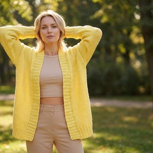 Puede incluir: Una mujer con un c&aacute;rdigan amarillo, un top corto beige y pantalones beige. El c&aacute;rdigan est&aacute; abierto, revelando el top y los pantalones. El fondo es un parque con &aacute;rboles y sol.