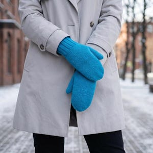 May include: A pair of bright blue knitted mittens. The mittens are a vibrant turquoise color and appear to be made of a soft, warm material. The mittens are worn with a light gray trench coat.