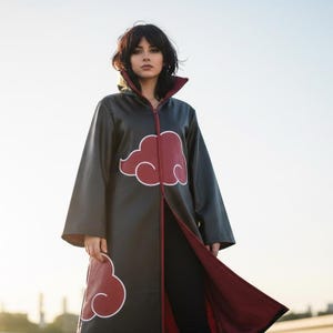 Op de afbeelding: Zwarte cosplay-cape met rode wolkenontwerpen en een rode binnenkant. De cape heeft een hoge kraag en een lange ritssluiting. Het ontwerp heeft een rode wolk met een witte omtrek.