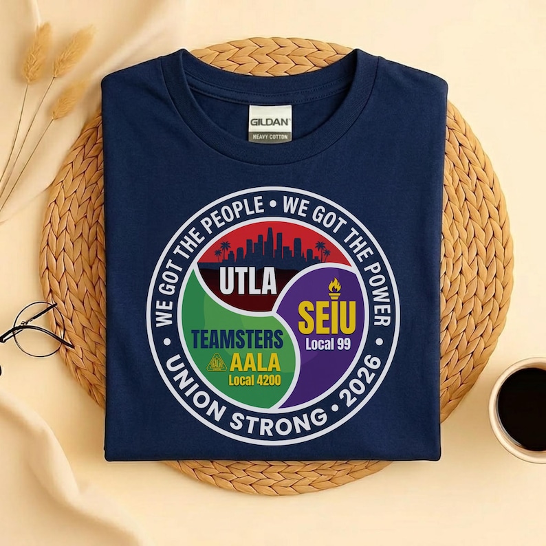 May include: Navy blue t-shirt with a round graphic featuring the text "WE GOT THE PEOPLE WE GOT THE POWER" and "UNION STRONG 2026". The graphic includes the logos of UTLA, Teamsters, AALA, and SEIU.