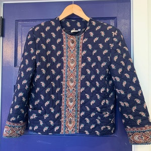 May include: A navy blue quilted jacket with a paisley print and a brown and teal patterned trim. The jacket has a button closure and two pockets.