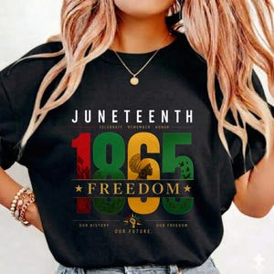 May include: A black t-shirt featuring the text JUNETEENTH, CELEBRATE REMEMBER HONOR, 1865, FREEDOM, OUR HISTORY, OUR FUTURE, OUR FREEDOM. The graphic includes a silhouette of a person with a headwrap and a raised fist icon in red, green, and gold.