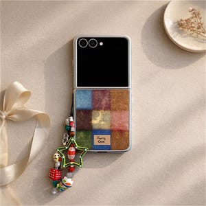 May include: A silver foldable phone case with a colourful, textured design. The case features a patchwork of squares in various colours, including blue, red, and gold. A charm with beads and a star is attached. The text "Furry Case" is visible.