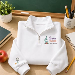 May include: A white quarter-zip sweatshirt featuring a graphic on the chest with a microscope, flowers, and the text Science TEACHER Mrs. Davis. The left sleeve includes a small magnifying glass and flower icon printed in a simple line style.