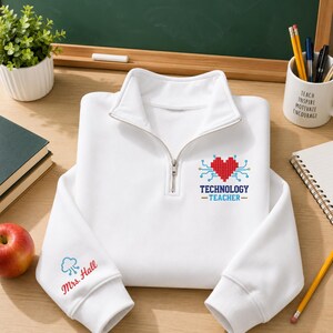 May include: A white quarter-zip sweatshirt featuring a red pixelated heart graphic with blue circuit lines and the text "TECHNOLOGY TEACHER" on the chest, and the text "Mrs. Hall" with a blue cloud icon on the sleeve cuff.