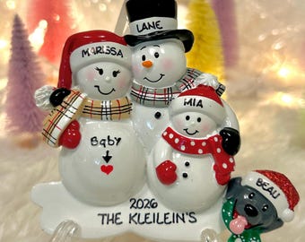 May include: A Christmas ornament featuring three snowmen and a dog. The snowmen are named Marissa, Lane, and Mia. The dog is named Beau. The ornament is inscribed with 2026 and THE KLEILEIN'S. The snowmen wear hats and scarves, and the dog wears a red hat.