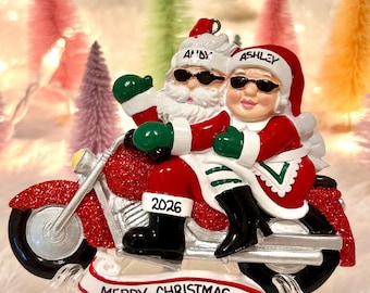 May include: A Christmas ornament featuring Santa and Mrs. Claus riding a red glittery motorcycle. They wear sunglasses and Santa hats labeled Andy and Ashley. The motorcycle has 2026 printed on the side, and a banner below reads MERRY CHRISTMAS.