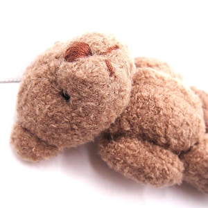 Könnte beinhalten: Ein kleiner, hellbrauner Plüsch-Teddybär mit einer flauschigen, strukturierten Oberfläche. Der Bär hat eine dunkelbraun gestickte Nase und einen Mund sowie kleine, dunkle, runde Augen. Die Gliedmaßen sind abgerundet und an einem weichen Körper.