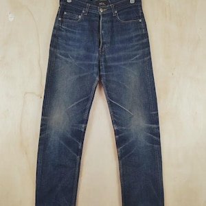 May include: A pair of dark blue denim jeans with a high-waisted fit and a button-fly closure. The fabric features natural fading patterns around the thighs and knees, with a straight-leg cut and a branded label on the interior waistband.