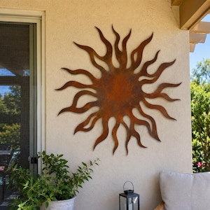 Peut inclure: Une décoration murale en métal circulaire en forme de soleil avec des rayons ondulés semblables à des flammes s'étendant depuis un centre plein. L'objet présente une finition patinée brun rouillé avec des tons orange foncé et clair.