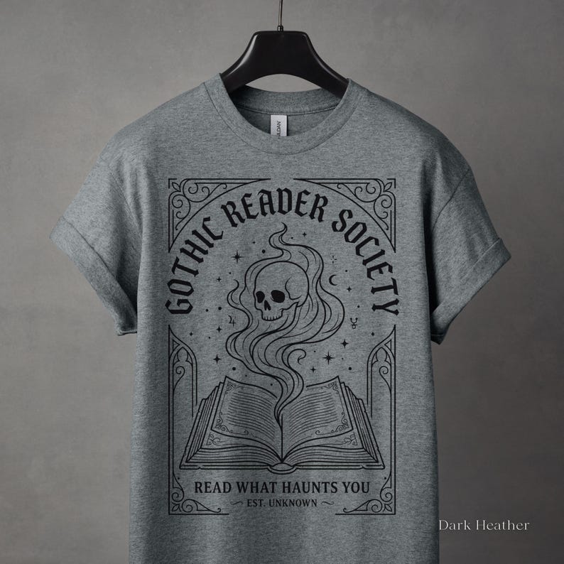 May include: Dark heather gray t-shirt featuring a graphic design for the "Gothic Reader Society." The design includes a skull with smoke rising from an open book, surrounded by text that reads "Read What Haunts You."