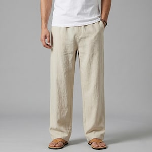May include: Beige linen trousers with a relaxed fit. The trousers have a straight leg design and a drawstring waist. The model is wearing brown sandals. The trousers are made of a lightweight fabric, ideal for warm weather.