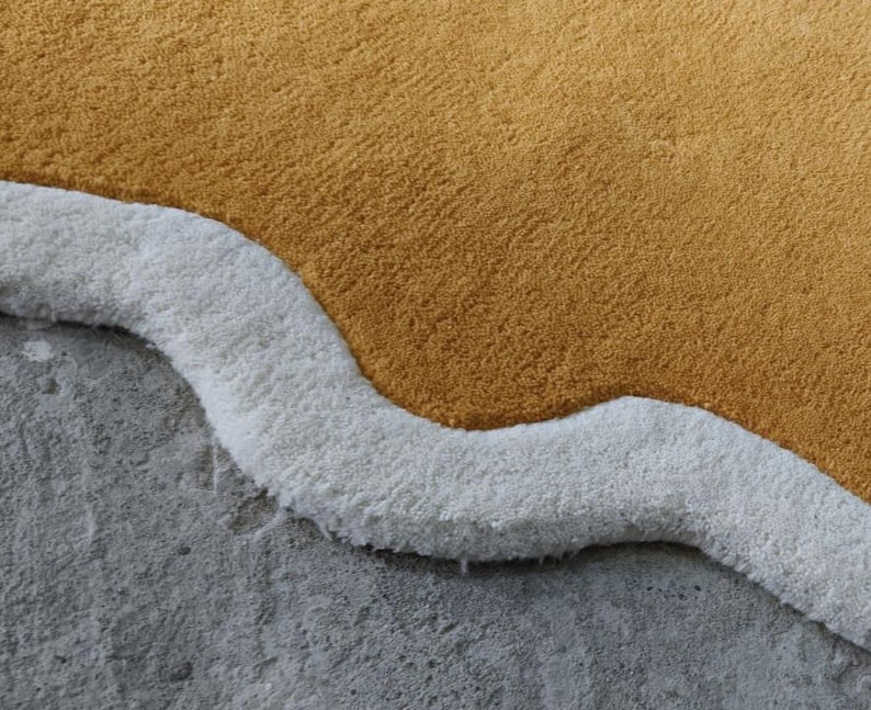 May include: A tufted rug featuring a large, solid mustard yellow section bordered by a thick, wavy white trim. The rug has a dense, plush pile texture and an irregular, organic shape that follows the curves of the white border edge.