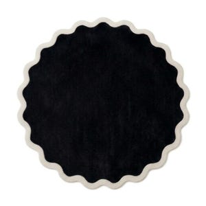 May include: A circular rug featuring a solid black center and a scalloped edge finished with a thick, cream-colored border. The design is symmetrical, with a soft, textured surface that creates a distinct contrast between the dark interior and light trim.