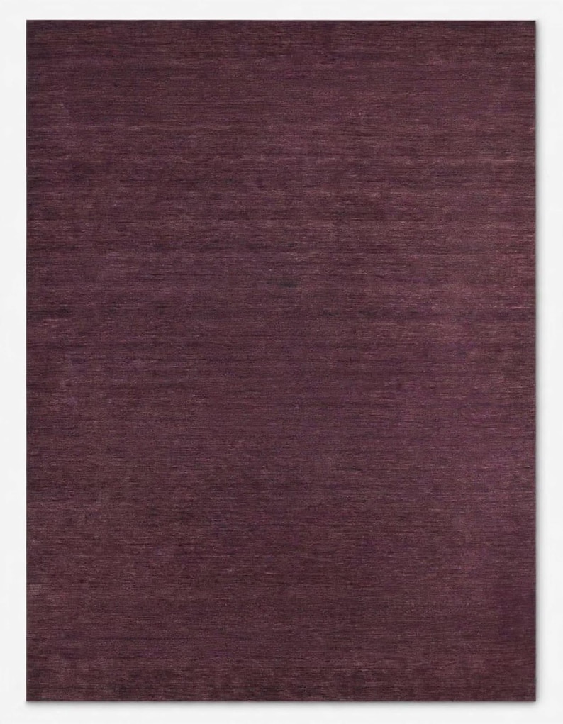 May include: A rectangular area rug in a deep, solid plum purple color. The surface features a consistent, fine-grained horizontal texture throughout, creating a subtle variation in light and shadow across the flat, woven fabric construction.