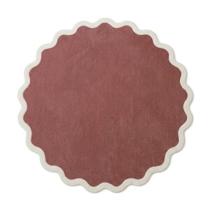 May include: A circular rug featuring a solid dusty rose center and a scalloped edge finished with a thick cream-colored border. The textile surface has a uniform, soft texture throughout, creating a distinct contrast between the muted pink and the light neutral trim.