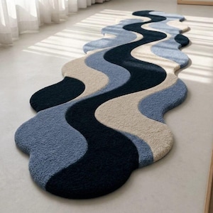 Pode incluir: Um tapete passadeira longo e estreito com uma forma orgânica ondulada. O tapete tem uma superfície texturizada e tufada com faixas de cores fluidas e repetitivas em azul-marinho profundo, azul-claro suave e um branco-creme macio.