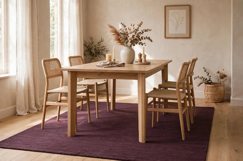 May include: A light wood rectangular dining table with four matching chairs featuring woven cane backrests and seats. The table is set with a ceramic vase containing dried foliage, two candles, and a small wooden salt and pepper shaker set.