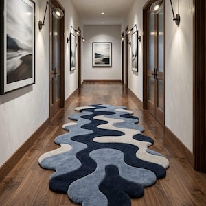 Pode incluir: Uma passadeira longa com uma forma ondulada org&acirc;nica e irregular, apresentando um padr&atilde;o em camadas em tons de azul-marinho escuro, azul m&eacute;dio e creme. O tapete tem um pelo espesso e texturizado, posicionado sobre um ch&atilde;o de madeira escura.