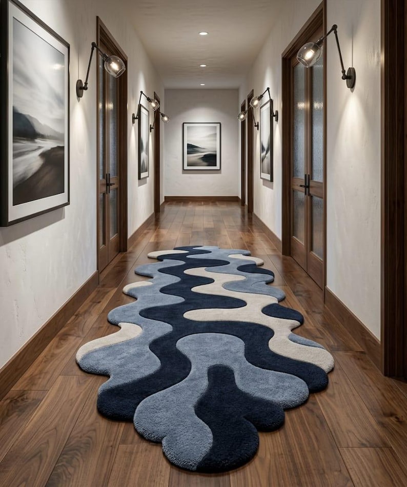Pode incluir: Uma passadeira longa com uma forma ondulada org&acirc;nica e irregular, apresentando um padr&atilde;o em camadas em tons de azul-marinho escuro, azul m&eacute;dio e creme. O tapete tem um pelo espesso e texturizado, posicionado sobre um ch&atilde;o de madeira escura.