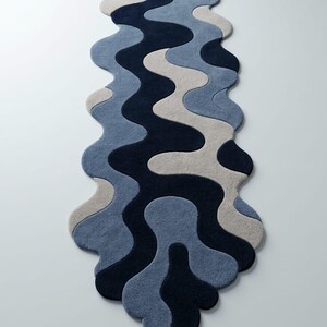 Pode incluir: Um tapete passadeira longo e estreito com uma forma org&acirc;nica ondulada e um padr&atilde;o em camadas de curvas entrela&ccedil;adas. O design consiste em blocos de cores s&oacute;lidas em azul-marinho profundo, azul-ard&oacute;sia m&eacute;dio e bege claro fluido.