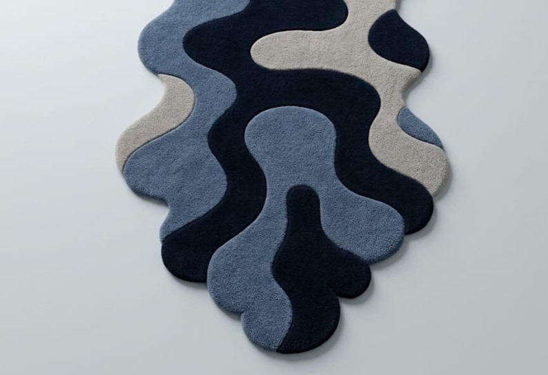 Pode incluir: Um tapete com formato org&acirc;nico irregular e textura tufada. O design consiste em padr&otilde;es fluidos e interligados em tons de azul-marinho escuro, azul m&eacute;dio e bege claro, criando uma apar&ecirc;ncia abstrata e em camadas.