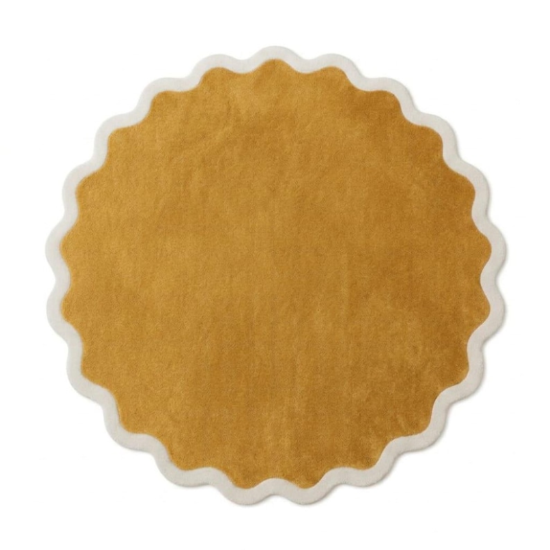 May include: A circular rug featuring a solid mustard yellow center with a soft, textured pile. The rug is framed by a distinct, scalloped edge border in a contrasting off-white color, creating a wavy, decorative outline around the entire perimeter.
