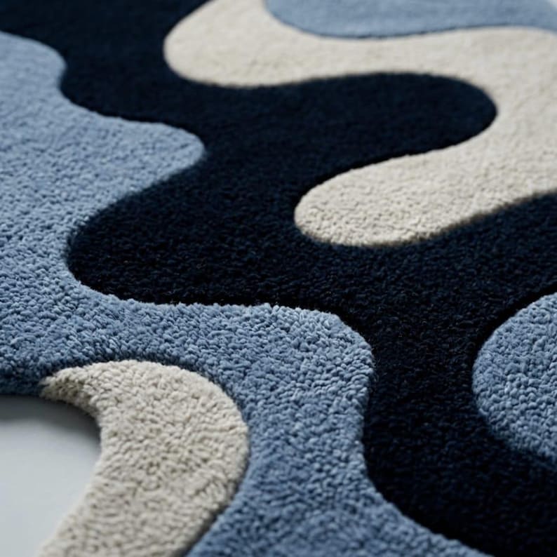 Pode incluir: Um tapete tufado com um padr&atilde;o abstrato ondulado de faixas grossas e interligadas em azul-marinho profundo, azul-claro suave e creme. A superf&iacute;cie possui um pelo denso e texturizado que cria um efeito de relevo entre as cores.