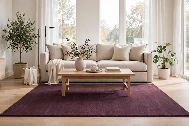 May include: A rectangular area rug in a deep, solid plum purple color with a subtle, low-pile texture. The rug is positioned on a light-toned wooden floor, providing a bold, dark contrast to the neutral-colored furniture and decor items placed above it.