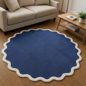 May include: A circular area rug featuring a solid deep blue center and a thick, cream-colored scalloped border. The rug has a soft, textured pile surface and is laid flat on a wooden floor, showcasing a distinct wavy edge design throughout.