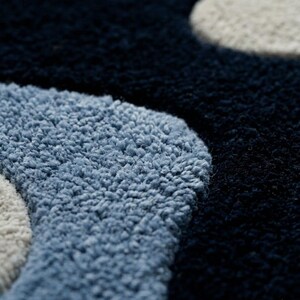 Pode incluir: Um tapete tufado com uma textura de pelo alto e um padr&atilde;o de formas org&acirc;nicas arredondadas. O design consiste em sec&ccedil;&otilde;es de azul-marinho profundo, azul-claro suave e branco-sujo, criando uma superf&iacute;cie densa e felpuda com &aacute;reas coloridas.