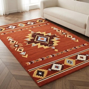 Op de afbeelding: Een rechthoekig vloerkleed met een diepe terracotta oranje basiskleur, voorzien van een centraal geometrisch medaillon en herhalende randpatronen in tinten crème, donkerbruin, lichtblauw en geel, gerangschikt in een symmetrisch ontwerp.
