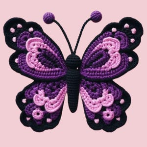 Op de afbeelding: Een handgemaakte gehaakte vlinder in tinten paars, roze en zwart. De vlinder heeft ingewikkelde vleugelpatronen en delicate antennes. De vleugels zijn ongeveer 20 cm breed, met een zwart lichaam en een roze achtergrond.