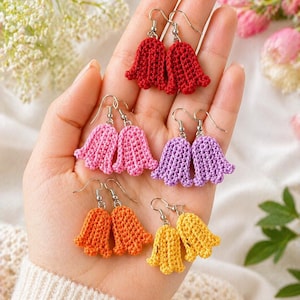 Op de afbeelding: Zes paar gehaakte oorbellen in belvorm in verschillende kleuren. De oorbellen hebben zilveren haken en zijn in rood, roze, paars, oranje en geel. De oorbellen worden getoond tegen een zachte achtergrond met bloemaccenten.