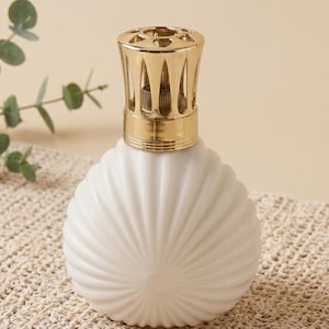 May include: A round, white ceramic fragrance lamp with a ribbed, shell-like texture. The top features a shiny, metallic gold-colored vented cap with a circular opening, designed to sit securely on the neck of the spherical white vessel.