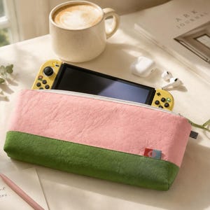 May include: A pink and green pencil case with a zipper, holding a yellow game console. A cup of coffee and a magazine are in the background. The text "Every moment matters" is on a small card.