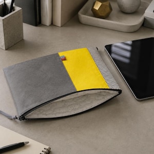 Könnte beinhalten: Eine rechteckige Reißverschlusstasche mit einem Color-Block-Design, bestehend aus einem großen grauen Bereich, einem leuchtend gelben Mittelteil und einer schwarz-weiß gestreiften Seite. Das Innere ist mit weißem Stoff mit grauen Sprenkeln gefüttert.