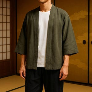 Può includere: Giacca verde oliva in stile kimono con maniche a tre quarti. La giacca è aperta sul davanti, rivelando una maglietta bianca. Il modello indossa pantaloni neri. Lo sfondo presenta porte scorrevoli in stile giapponese tradizionale.