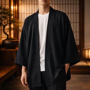 Puede incluir: Chaqueta negra estilo kimono con mangas anchas, usada sobre una camiseta blanca. La chaqueta tiene un corte holgado y la parte delantera abierta. El fondo presenta un interior tradicional japonés.