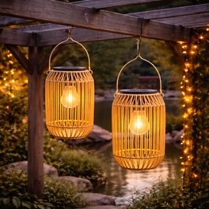 Peut inclure: Deux lanternes solaires suspendues avec un design en forme de bambou. Chaque lanterne contient une ampoule chaude et brillante et est suspendue à une pergola en bois. L'arrière-plan présente un étang et une végétation luxuriante.