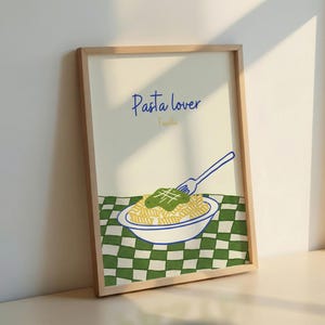 May include: A framed art print featuring a pasta dish illustration. The artwork includes a bowl of fusilli pasta with pesto, a fork, and the text "Pasta lover." The background has a green and white checkered pattern.