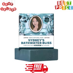Könnte beinhalten: Ein dunkelblaues Seifenstück liegt unter einer Schachtel mit der Aufschrift "Sydney's Bathwater Bliss". Die Schachtel zeigt eine Illustration einer Frau und den Text "Limited Men's Natural Soap Edition". Die Seife wiegt 141g.