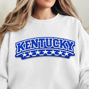 Può includere: Una tazza di ceramica bianca con manico nero e la scritta "But First, Coffee" in nero, con un carattere a mano. La tazza è su una superficie bianca.